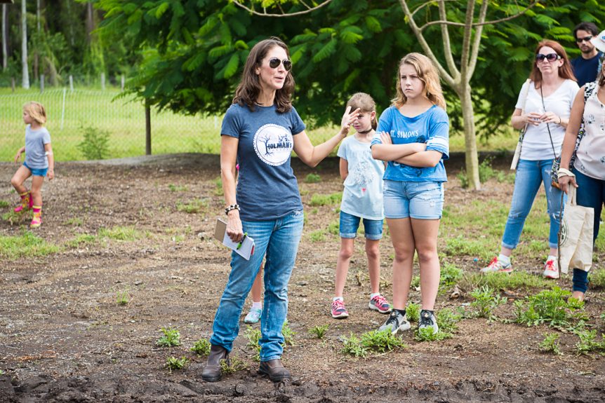 A woman is talking to a group of children in the dirt.
