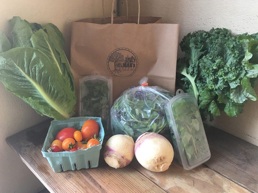 A bag of vegetables and fruit sits on a wooden table.